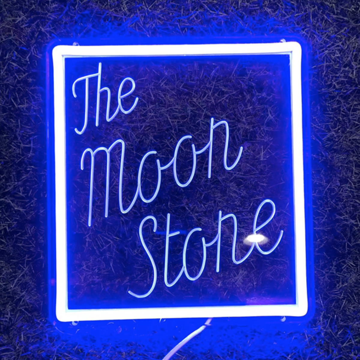 A neon sign that reads 'The Moon Stone' in a square frame with a blue background.
